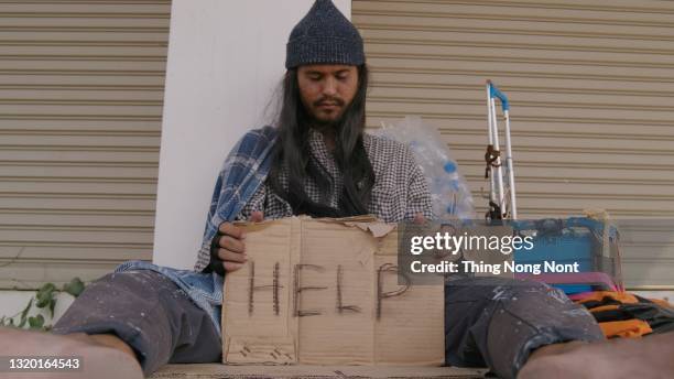 homeless man sitting on the street in the shadow of the building and begging for help and money. problems of big modern cities. - big bums fotografías e imágenes de stock