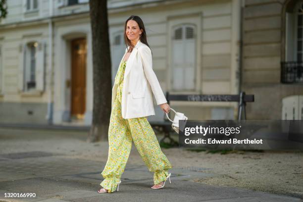 Alba Garavito Torre wears gold earrings, a green with white daisy pattern Mirae jumpsuit with off shoulder knotted neck and puffy ankles, a white...