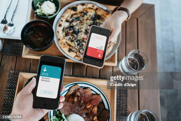 high angle view of friends splitting bill, sending / receiving the payment of the meal through digital wallet device on smartphone while dining together in a restaurant - restaurant bill ストックフォトと画像