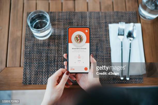 overhead view of young asian woman placing a food order and making contactless mobile payment with mobile app on smartphone in a restaurant. eating out lifestyle. contactless menu ordering and payment concept - shopping screen stock-fotos und bilder