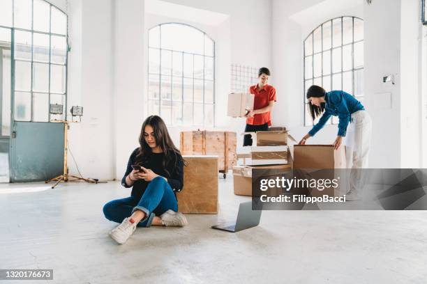 a young adult woman is looking her smartphone in a new loft office - business start up stock pictures, royalty-free photos & images