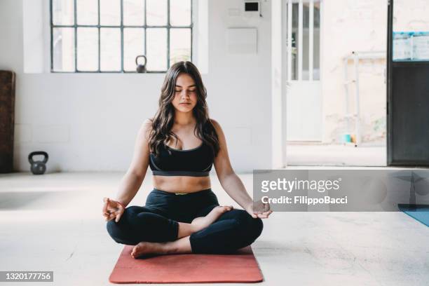 la giovane donna adulta pratica yoga in un loft moderno - meditation sitting foto e immagini stock