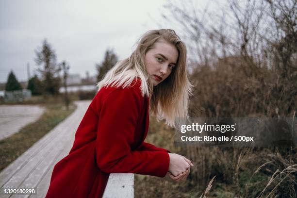 young woman in red jacket standing by railing in nature - editorial - fotografias e filmes do acervo