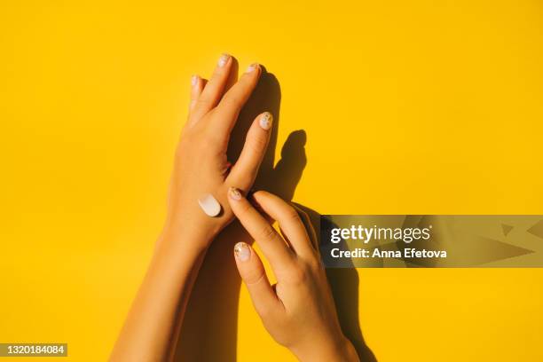 woman is spread cream on hands with manicure against illuminating yellow background. body care concept. trendy colors of the year 2021. flat lay style - applying stock photos et images de collection