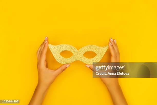 woman hands with manicure with gold smears are holding gold carnival mask on illuminating yellow background. trendy colors of the year 2021. flat lay style. copy space for your design - masquerade mask stock pictures, royalty-free photos & images