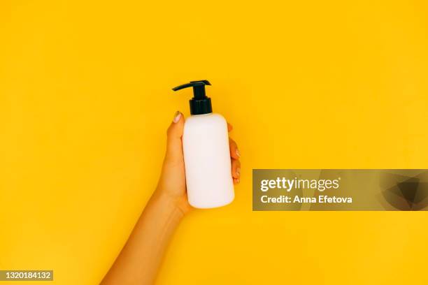 woman hands with manicure are holding white plastic bottle with dispenser on illuminating yellow background. trendy colors of the year 2021. flat lay style. copy space for your design - shampoo bottle white background stock-fotos und bilder