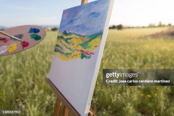 hands holding paintbrush and color palette while painting rural landscape - art easel stock-fotos und bilder