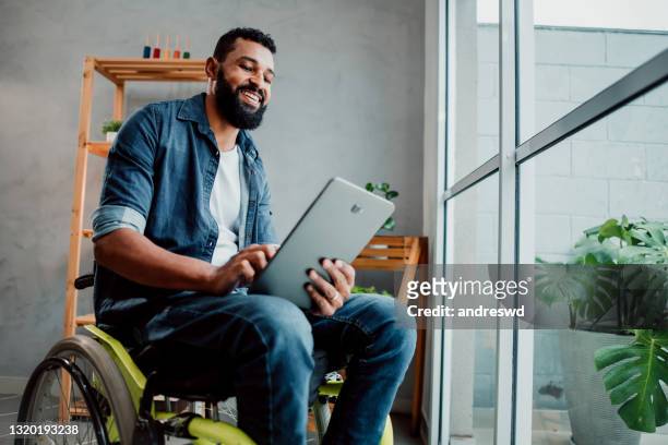 man in a wheelchair using digital tablet - man in wheelchair stock pictures, royalty-free photos & images