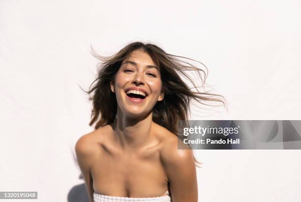 young brunette woman laughing while enjoying wellness and sun, in front of a white wall - sleeveless top stock pictures, royalty-free photos & images