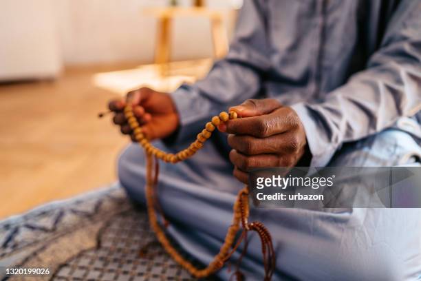 muslimischer mann hält gebetsperlen während des gebets - islam stock-fotos und bilder