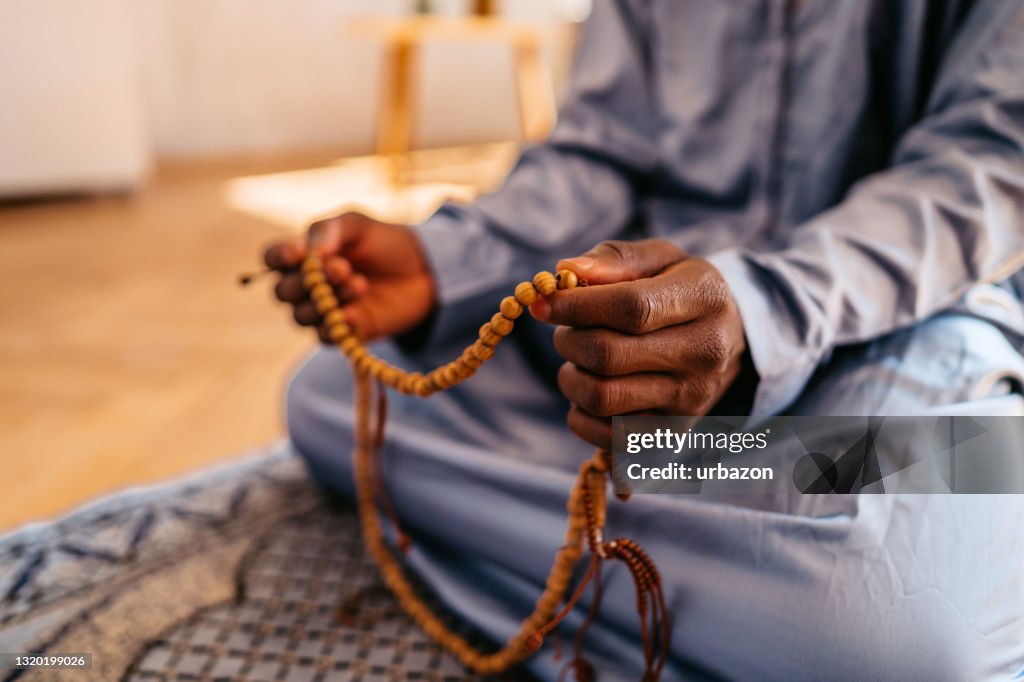 Muslim man holding prayer beads while praying