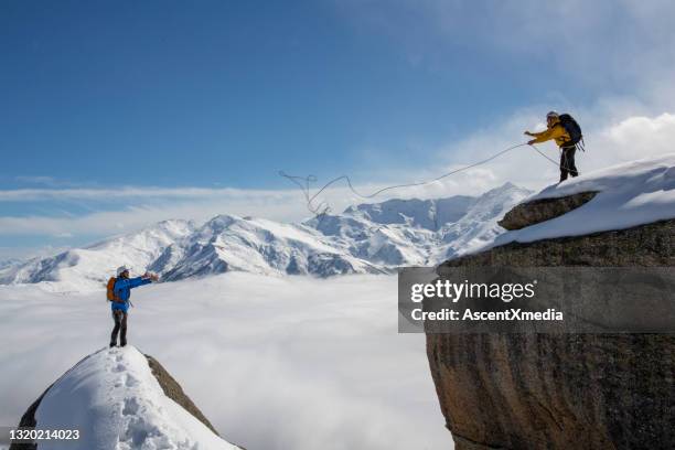 mountaineer throws rope to partner from summit - rope high rescue imagens e fotografias de stock