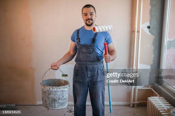 smiling painter in coveralls holding paint roller and a bucket - decorating stock pictures, royalty-free photos & images