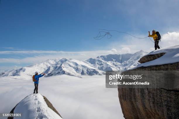 mountaineer throws rope to partner from summit - rope high rescue imagens e fotografias de stock