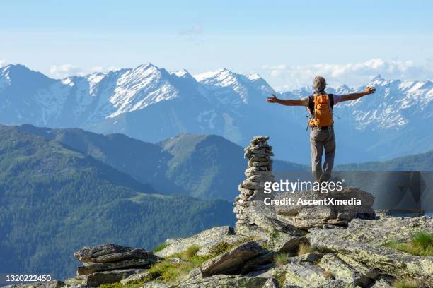 hiker outstretches arms on sunny mountain summit by rock cairn - on top of mountain stock pictures, royalty-free photos & images