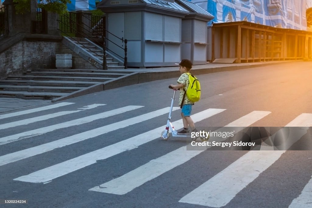 A Boy With A Backpack Crosses The Road On A Zebra Crossing On A Scooter  High-Res Stock Photo - Getty Images