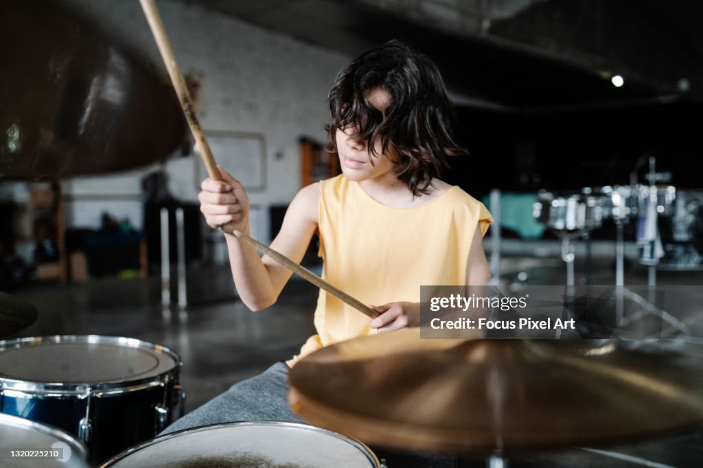Teenage drummer in tank top playing the drums looking away