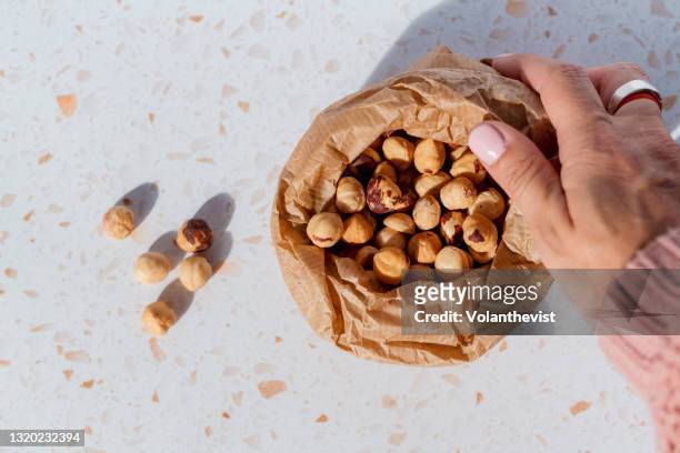 bulk organic hazelnuts in a brown paper bag on a terrazzo marble - single seed stock pictures, royalty-free photos & images
