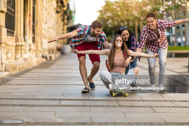 glückliche gruppe von schülern hat viel spaß beim fahren auf einem skateboard in einer city street - international student day stock-fotos und bilder