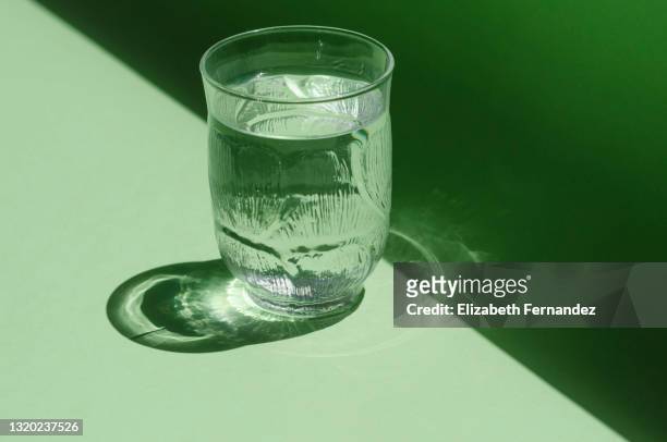 close-up of a glass of water shining in the sunlight on a bright green background. - drinking glass stock pictures, royalty-free photos & images