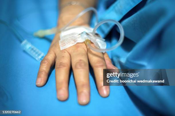 close up of the saline tube on the left hand of the patient is giving the saline solution that lies in the hospital bed. achoo, flu season. - infused 個照片及圖片檔