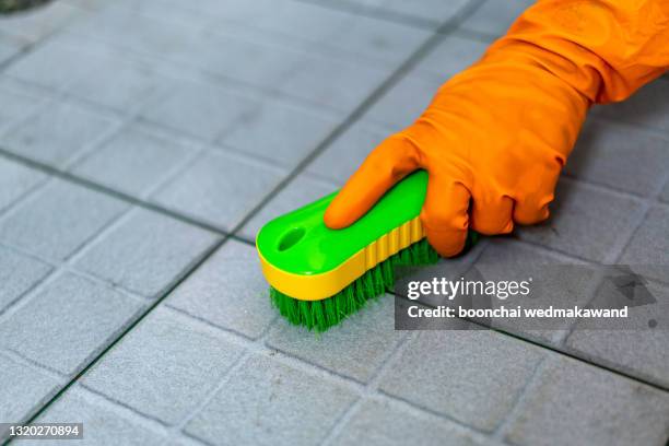 hand of man wearing orange rubber gloves is used to convert scrub cleaning on the tile floor. - washing up glove - fotografias e filmes do acervo