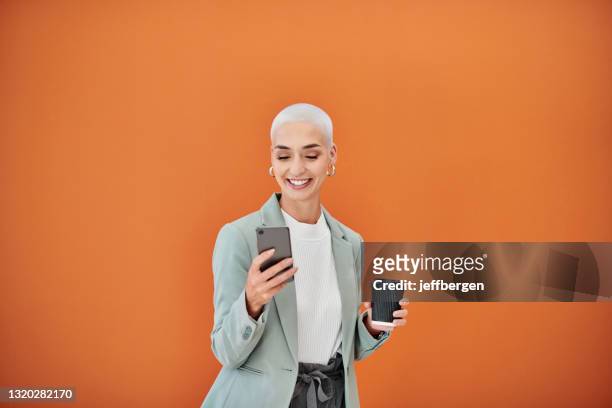 ontsproten van een jonge onderneemster die een cellphone tegen een oranje achtergrond met behulp van - blazer stockfoto's en -beelden
