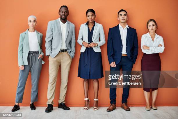 portrait of a group of businesspeople standing together against an orange background - dedication background stock pictures, royalty-free photos & images