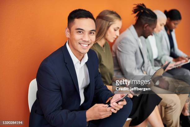 porträt eines jungen geschäftsmannes, der mit seinen kollegen im hintergrund ein handy vor orangefarbenem hintergrund benutzt - candidate stock-fotos und bilder