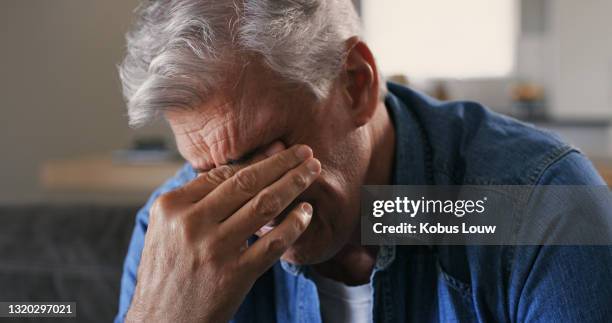 schuss eines reifen mannes, der allein auf dem sofa zu hause sitzt und gestresst aussieht - hand on head stock-fotos und bilder