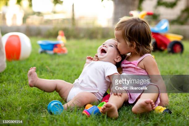happy smiling baby brother and toddler sister playing with toys together in backyard garden in summer season at sunset - theater performance outdoors stock pictures, royalty-free photos & images