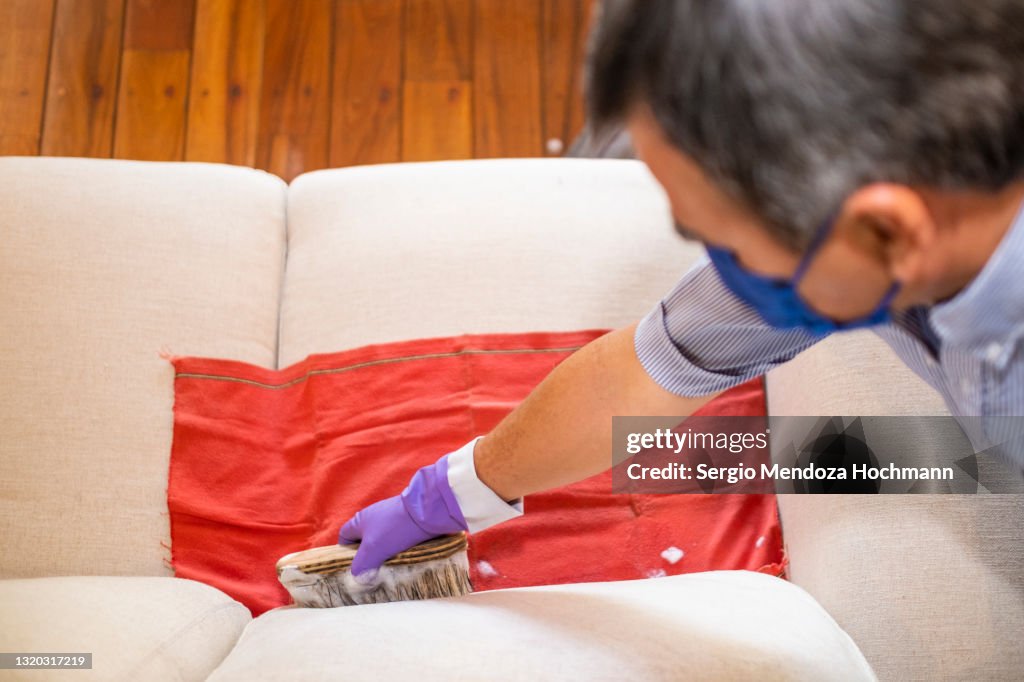 Latino man wearing a face mask during the COVID-19 pandemic cleans a sofa with a brush