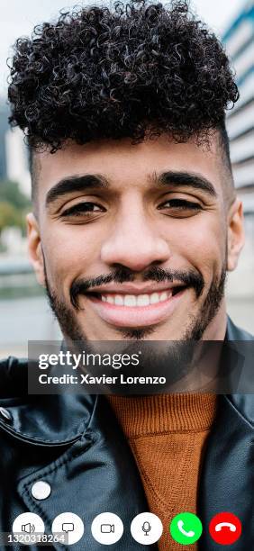 smiling hispanic man having a video call on mobile phone - vertical screen stock pictures, royalty-free photos & images