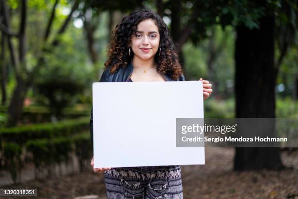 young latino woman with curly hair holding a blank sign, smiling - placard stock pictures, royalty-free photos & images