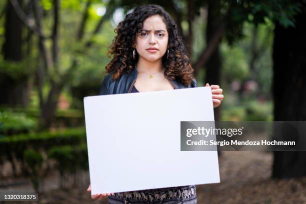 young latino woman with curly hair holding a blank sign, frowning - women only holding placards stock-fotos und bilder