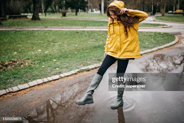 junge frau spielt bei regen - frau mit gelben regenmantel stock-fotos und bilder