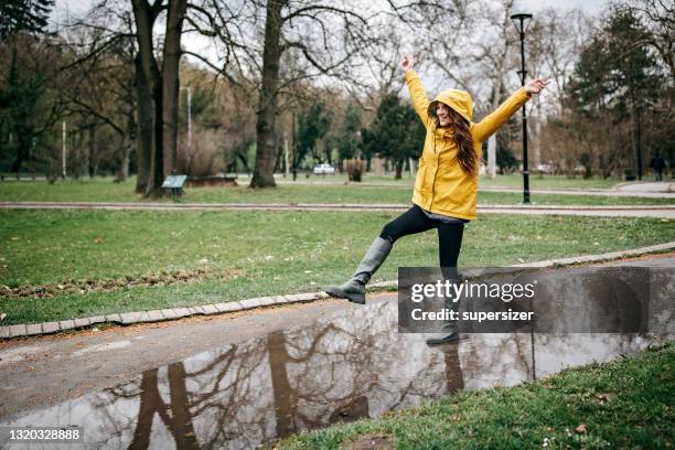 young woman plays during rain - raincoat stock pictures, royalty-free photos & images