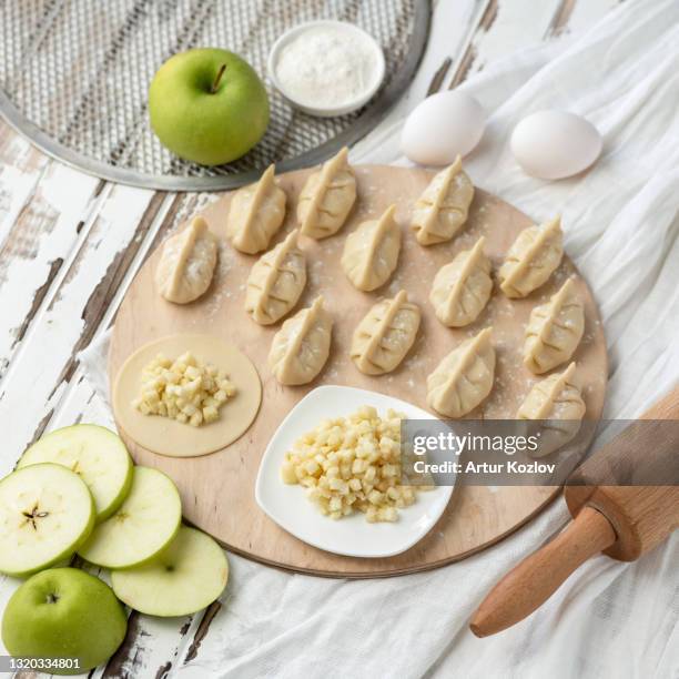 cooking process. sweet dumplings with green apple filling on raw dough circles at wooden cutting board. ingredients and rolling pin on rustic background. convenience food concept. flat lay - frozen apple fotografías e imágenes de stock