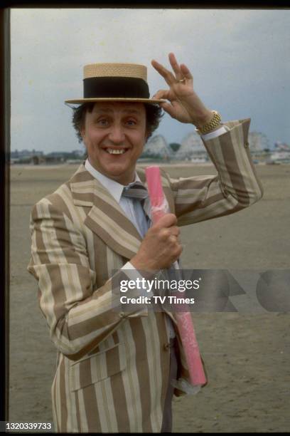 Entertainer Ken Dodd photographed on the beach with a stick of rock, circa 1980.