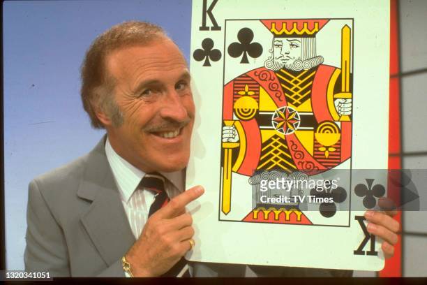 Host Bruce Forsyth holding an oversized king of clubs playing card on the set of game show Play Your Cards Right, circa 1980.