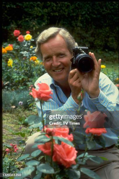 Radio and television presenter Nicholas Parsons photographing roses in a garden, circa 1983.