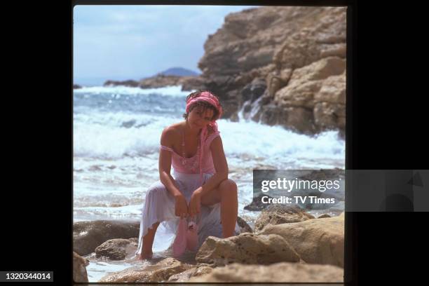 Actress Amanda Burton photographed sitting on a rocky beach in Benidorm, Spain, circa 1984.