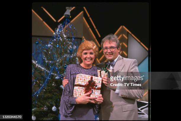 Hosts Cilla Black and Christopher Biggins holding Christmas gifts on the set of light entertainment series Surprise Surprise, circa 1984.