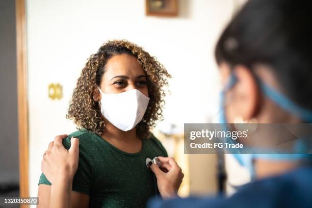 medico che ascolta il cuore del paziente a casa durante la visita a casa - indossando una maschera protettiva per il viso - protective face mask foto e immagini stock