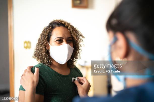 doctor listening to patient's heart at home during home visit - wearing protective face mask - máscara de proteção imagens e fotografias de stock