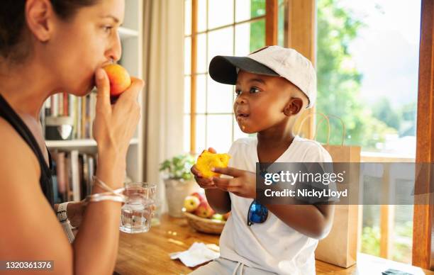 mom eating a peach with her cute little boy at home - foster care stock pictures, royalty-free photos & images