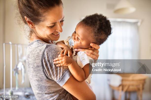 baby girl with a pacifier being held by her loving mom at home - adoption stock pictures, royalty-free photos & images