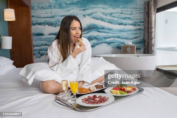 excited woman eating cake on hotel bed - hotel breakfast stock pictures, royalty-free photos & images