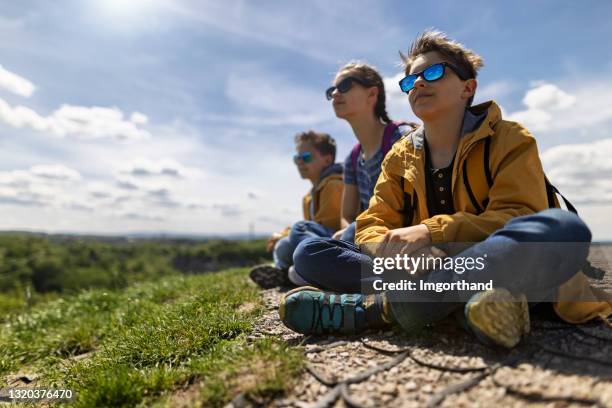 tre escursionisti bambini seduti sulla cima della collina e guardando la vista - family hiking in spring outdoors foto e immagini stock