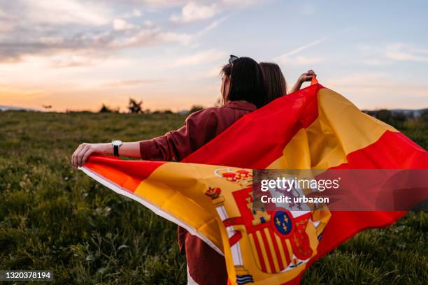 two women  covering themselves with spanish flag on meadow - spanish flag stock pictures, royalty-free photos & images